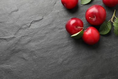 Photo of Delicious ripe cherry plums with leaves on black table, flat lay. Space for text