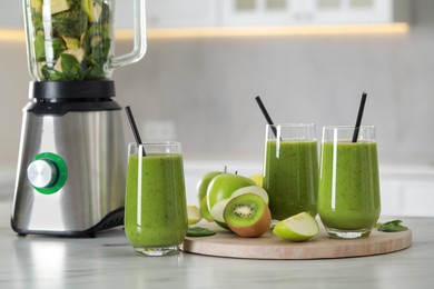 Photo of Delicious fresh smoothie and blender with ingredients on white marble table in kitchen