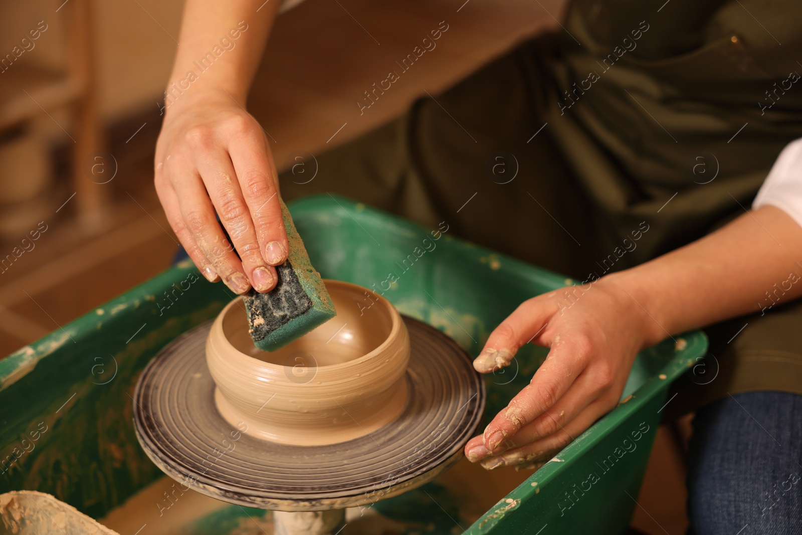 Photo of Clay crafting. Woman making bowl on potter's wheel indoors, closeup