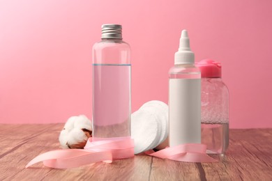 Photo of Composition with makeup removers and cotton pads on wooden table against pink background