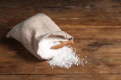 Photo of Bag of natural sea salt and scoop on wooden table. Space for text