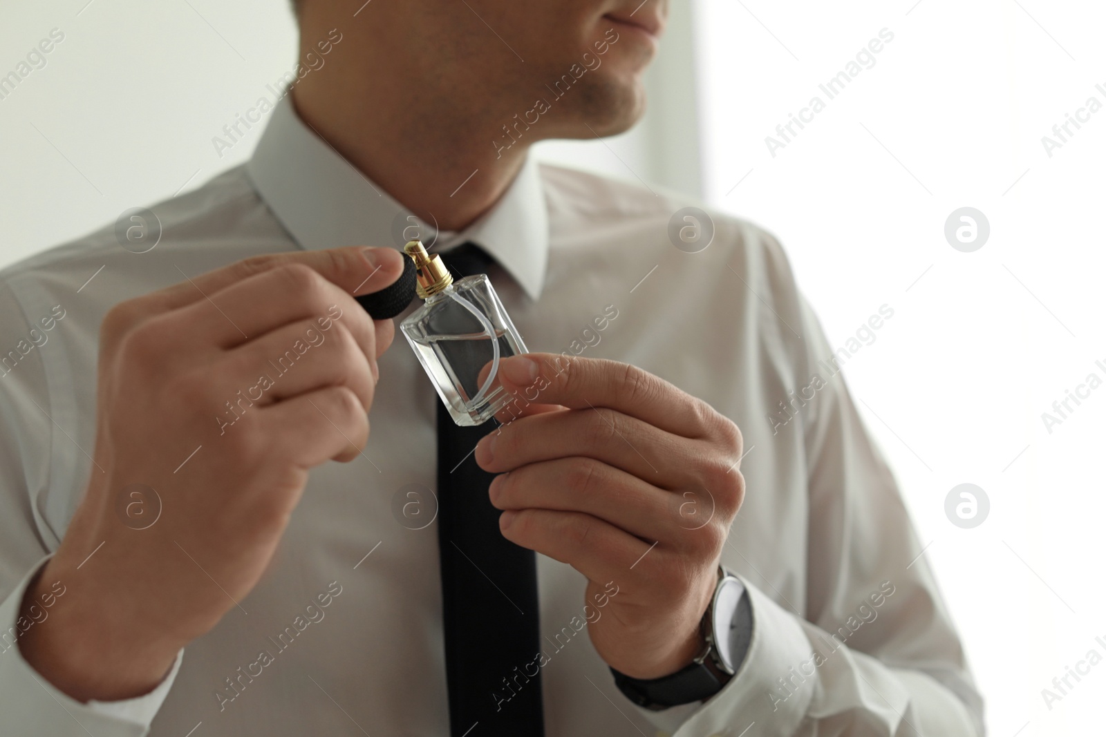 Photo of Handsome man applying perfume on neck indoors, closeup. Space for text