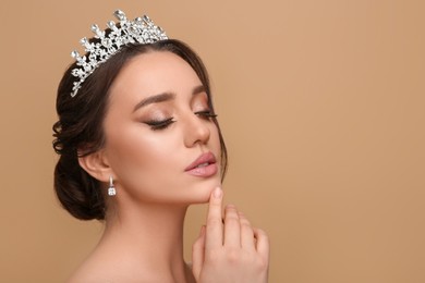 Beautiful young woman wearing luxurious tiara on beige background, space for text