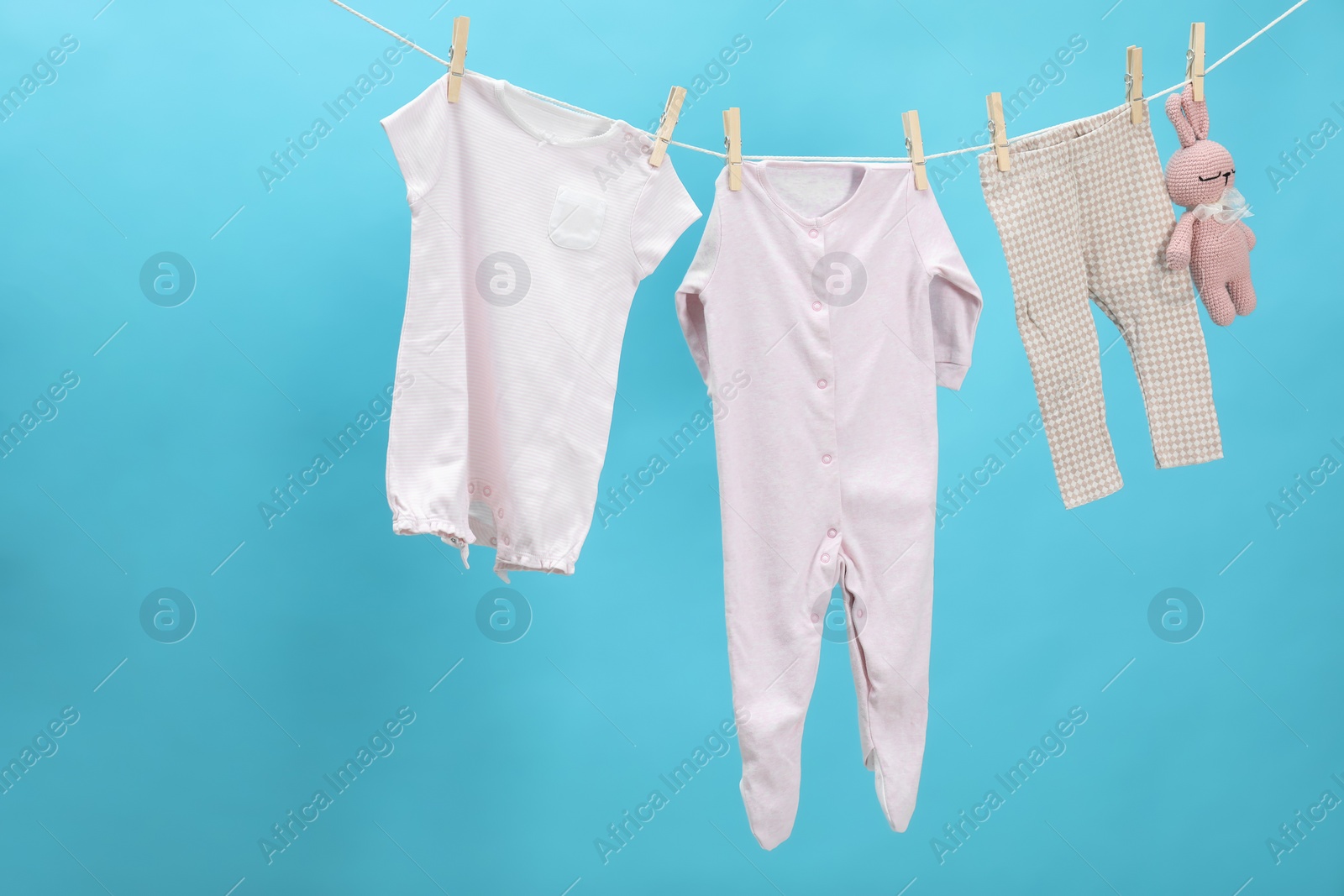 Photo of Different baby clothes and bunny toy drying on laundry line against light blue background