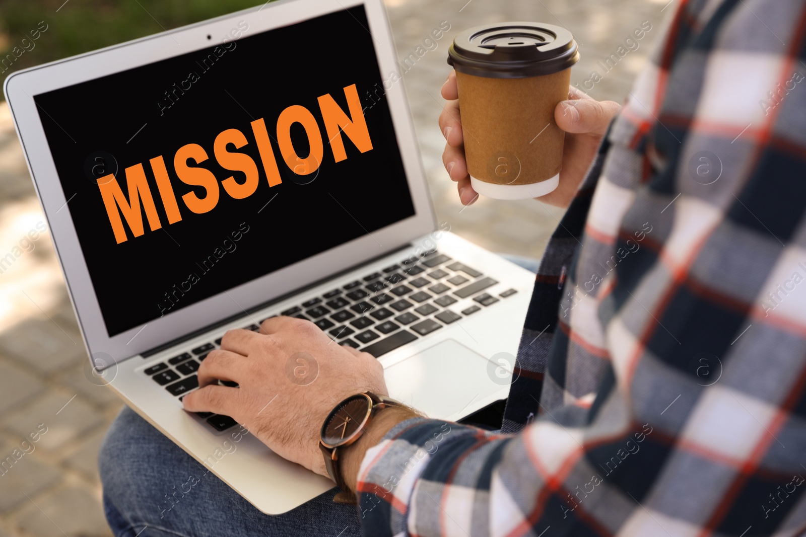 Image of Young man using modern laptop with word MISSION on screen outdoors, closeup 