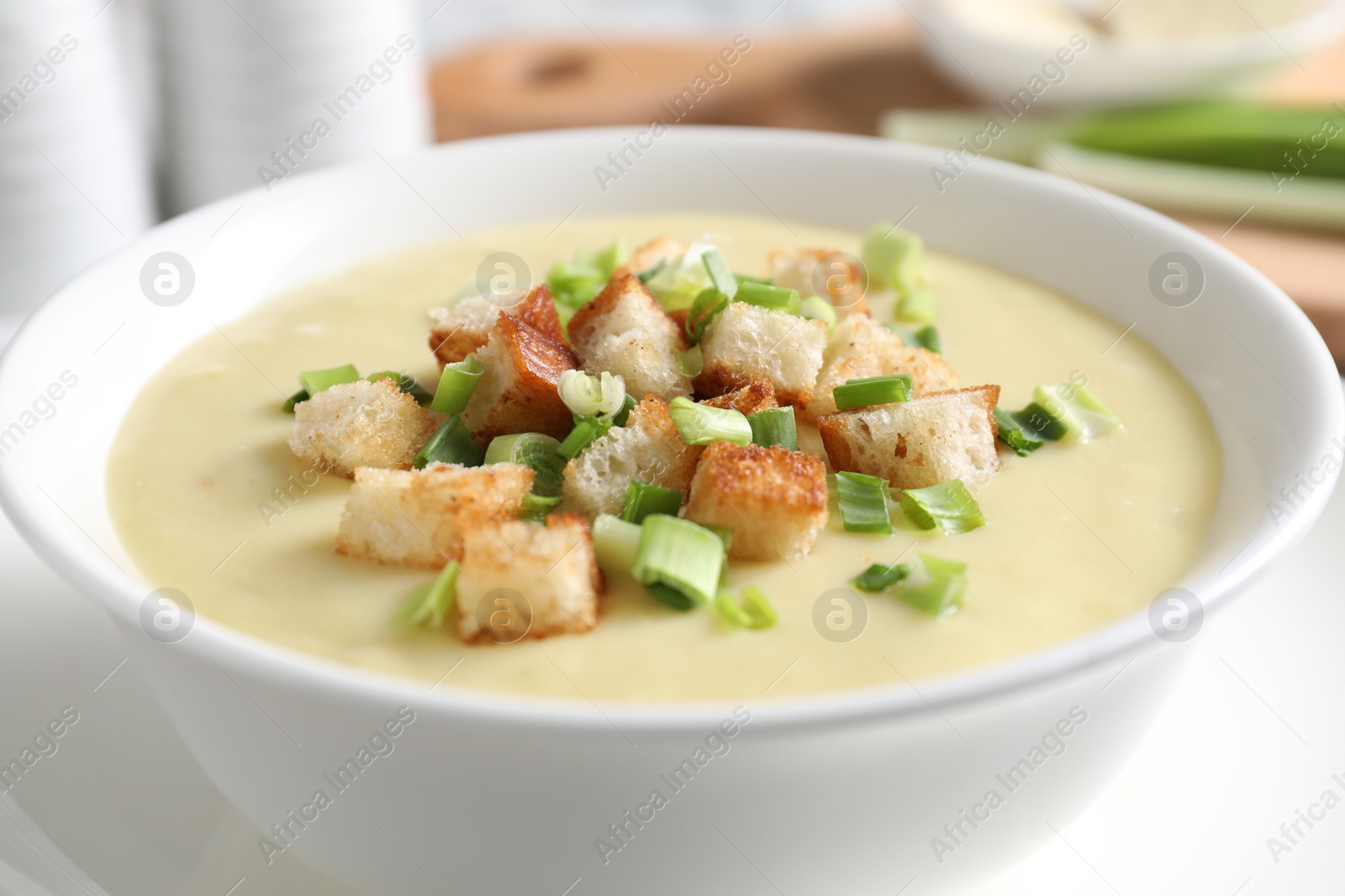 Photo of Tasty potato soup with croutons and green onion in bowl on white table, closeup