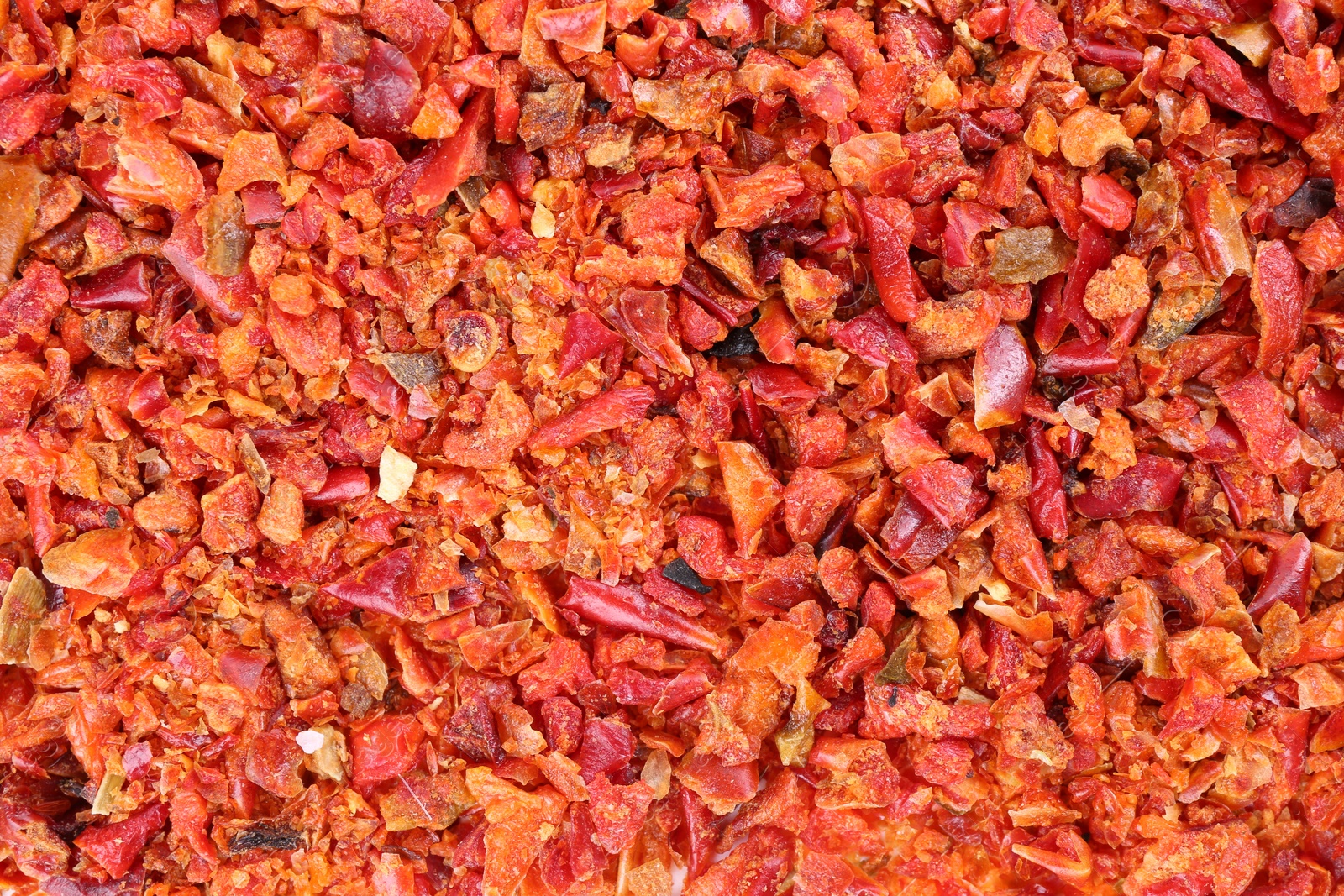 Photo of Aromatic spice. Red chili pepper flakes as background, top view