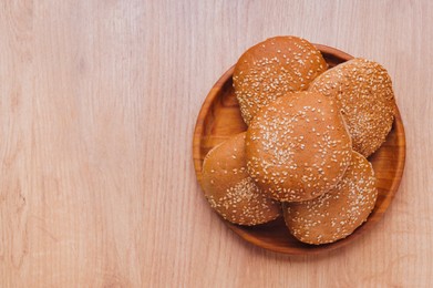 Photo of Fresh buns with sesame seeds on wooden table, top view. Space for text