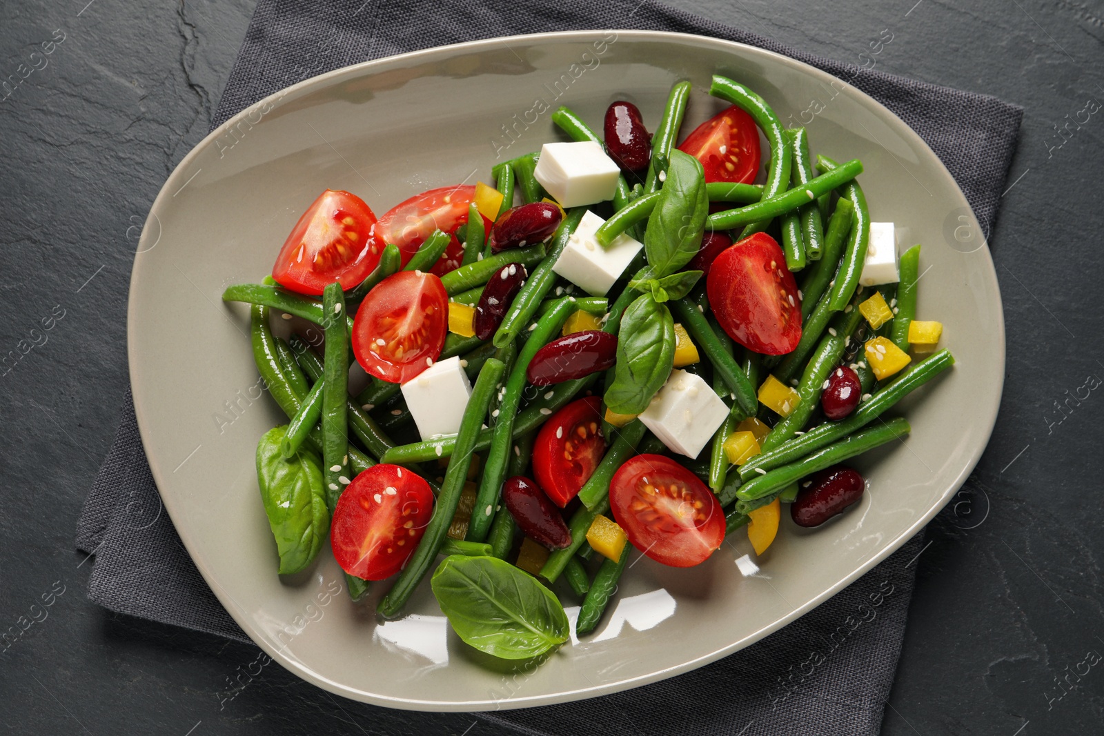 Photo of Plate of tasty salad with green beans on black table, top view