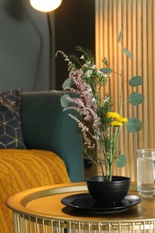 Photo of Stylish ikebana with beautiful flowers and green branches carrying cozy atmosphere at home