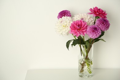 Photo of Bouquet of beautiful Dahlia flowers in vase on table near white wall, space for text