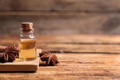 Bottle of essential oil and anise on wooden table. Space for text