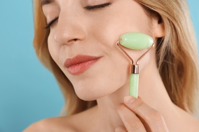 Photo of Young woman using natural jade face roller on light blue background, closeup
