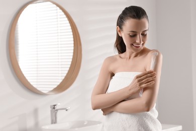 Happy woman applying body cream onto arm in bathroom, space for text