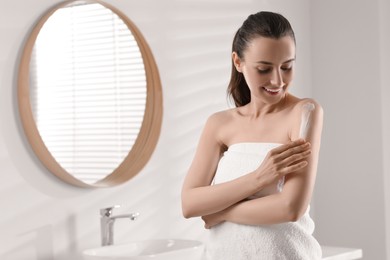 Photo of Happy woman applying body cream onto arm in bathroom, space for text