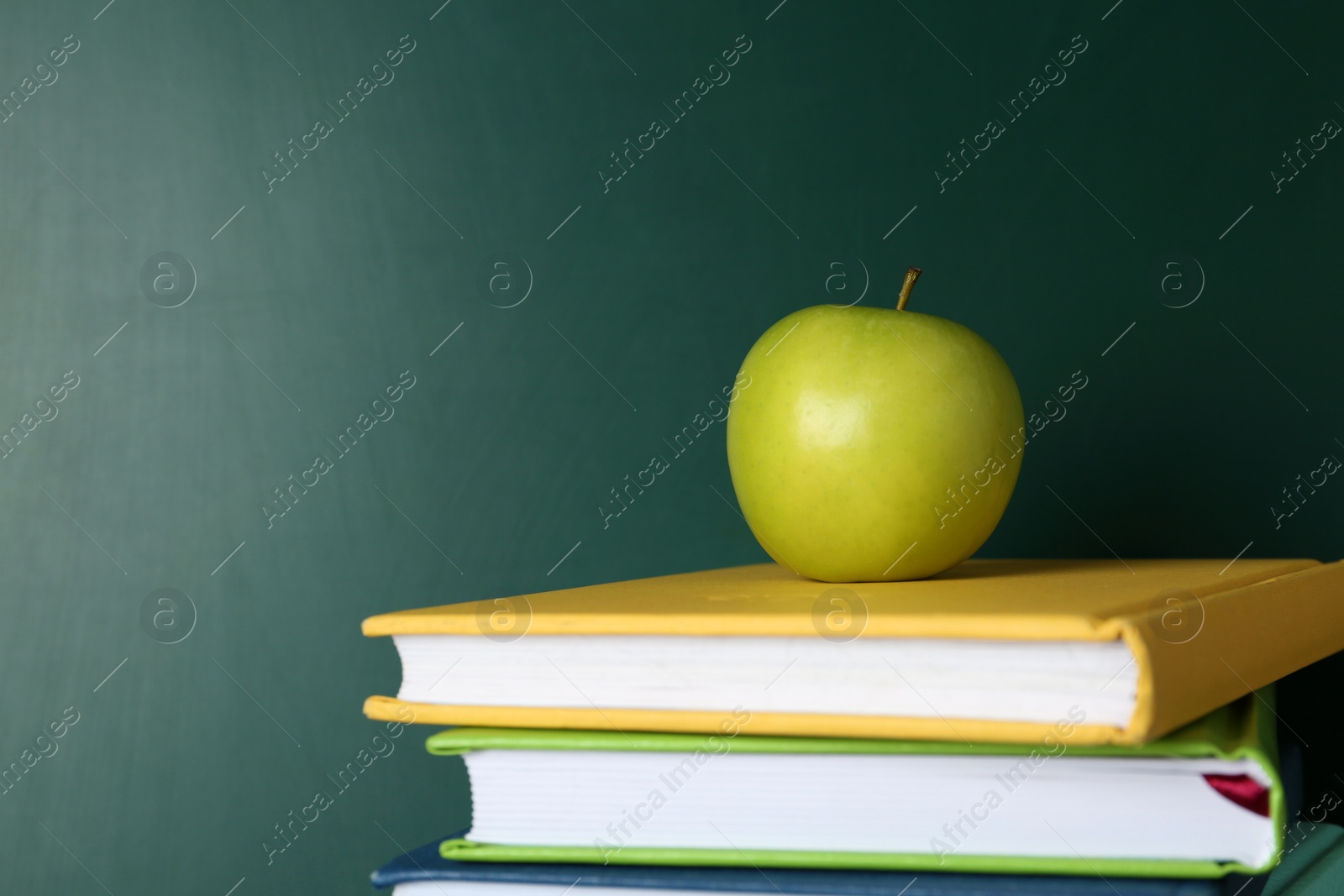 Photo of Books and apple near green chalkboard, space for text. School education