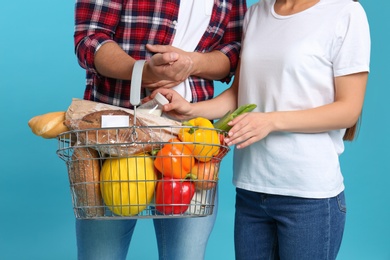 Photo of Young couple with shopping basket full of products on blue background, closeup