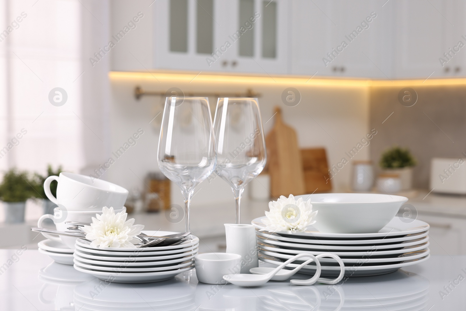 Photo of Set of clean dishware, glasses, cutlery and flowers on table in kitchen