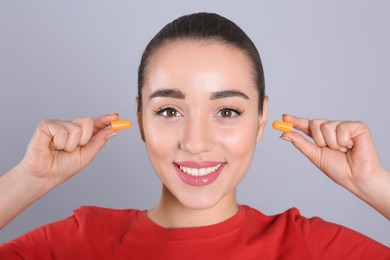 Photo of Young woman inserting foam ear plugs on grey background