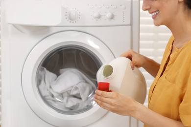 Photo of Woman pouring laundry detergent into cap near washing machine indoors, closeup