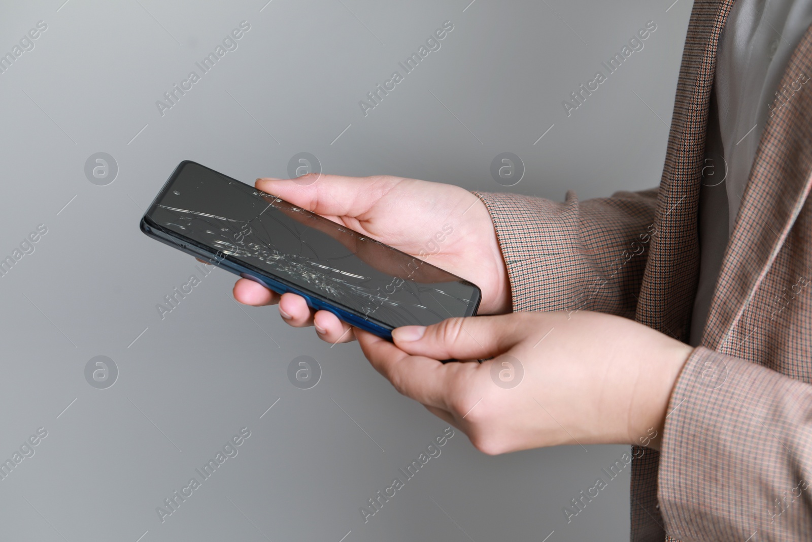 Photo of Woman holding damaged smartphone near light grey wall, closeup. Device repairing