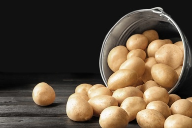 Photo of Raw fresh organic potatoes on black wooden table against dark background. Space for text