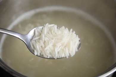 Photo of Spoon with cooked rice over pot, closeup
