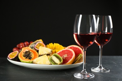 Delicious exotic fruits and glasses of wine on black table