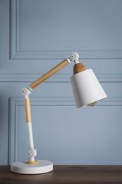 Photo of Stylish modern desk lamp on wooden table near light grey wall