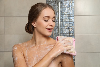 Photo of Young woman covered with soap foam taking shower in bathroom