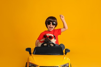 Photo of Little boy with his dog in toy car on yellow background