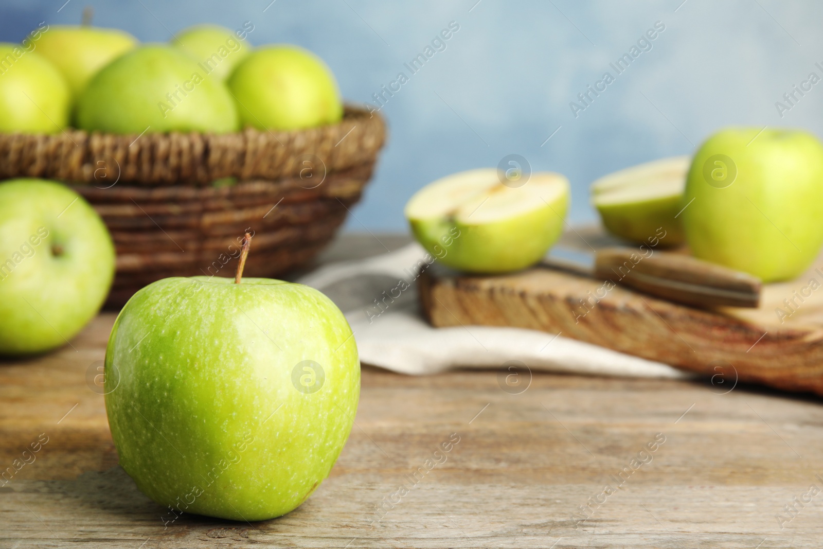 Photo of Fresh ripe green apple on wooden table against blue background, space for text