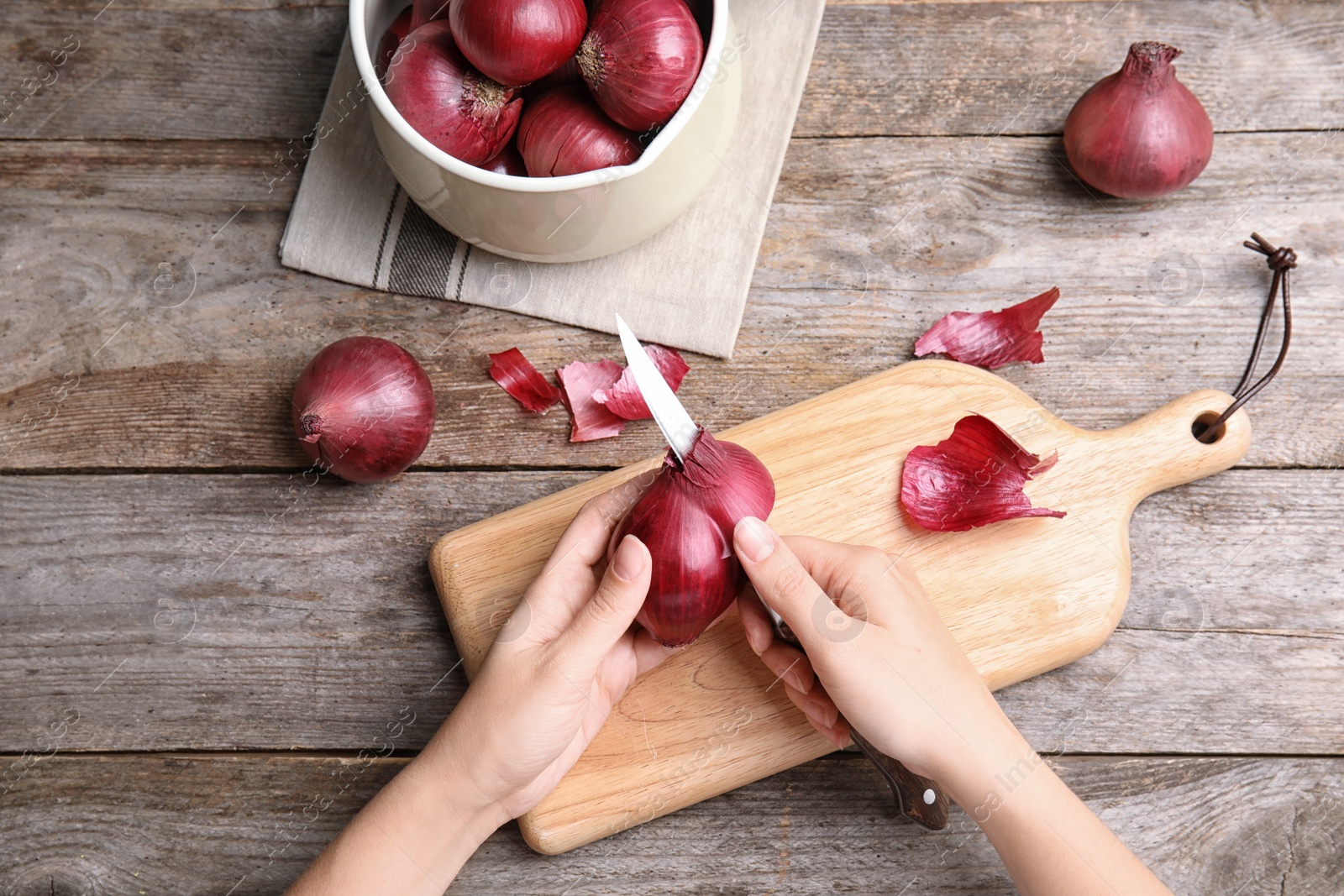 Photo of Woman peeling ripe red onion on wooden table, top view