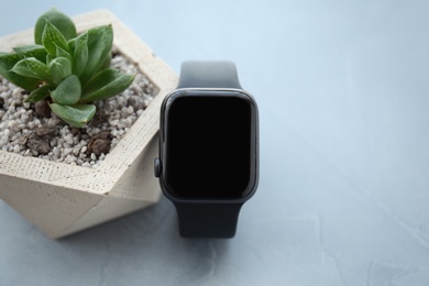 Photo of Stylish smart watch and plant on grey stone table, closeup. Space for text