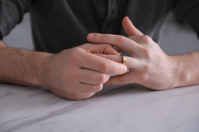 Photo of Man taking off wedding ring at white marble table, closeup. Divorce concept