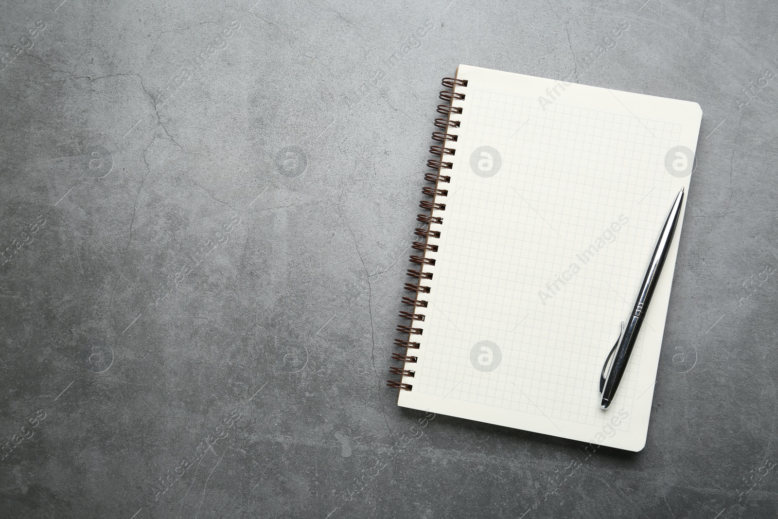 Photo of Notebook and pen on grey table, top view. Space for text