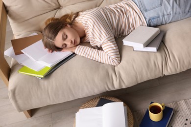 Photo of Young tired woman sleeping near books on couch indoors