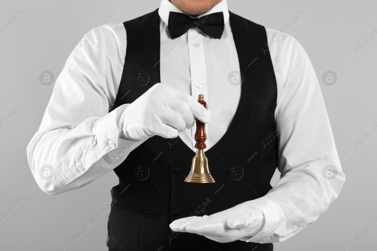 Photo of Butler holding hand bell on grey background, closeup