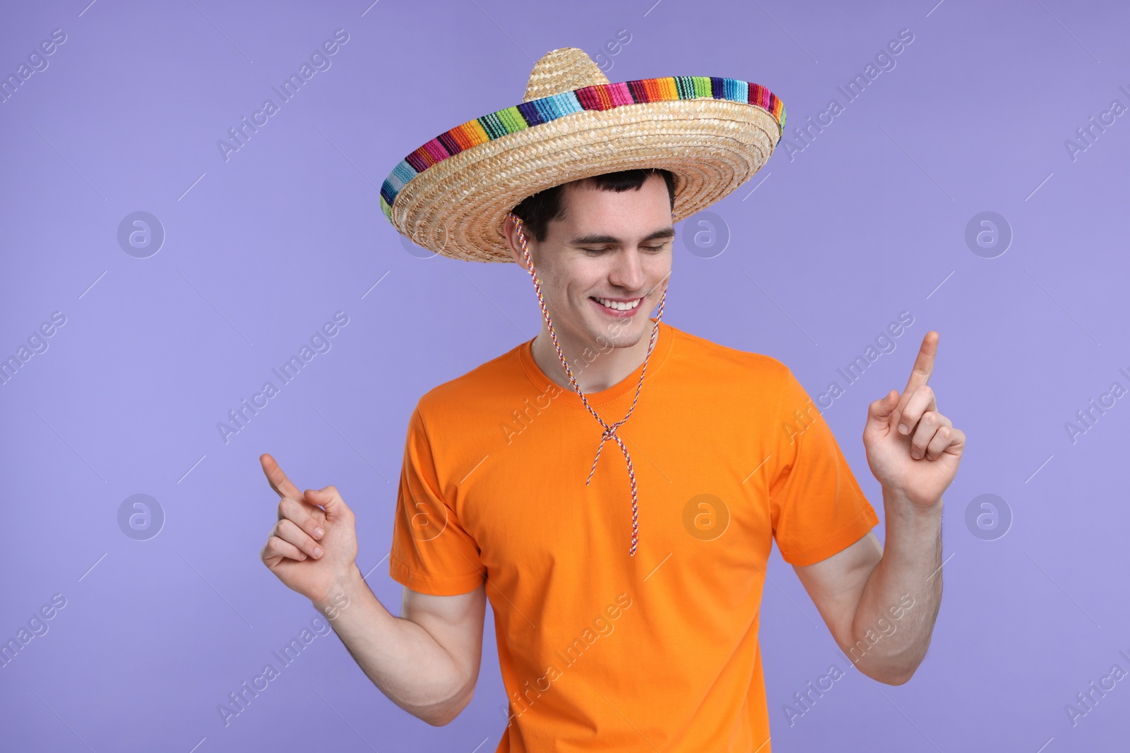 Photo of Young man in Mexican sombrero hat pointing at something on violet background