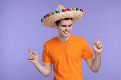 Photo of Young man in Mexican sombrero hat pointing at something on violet background