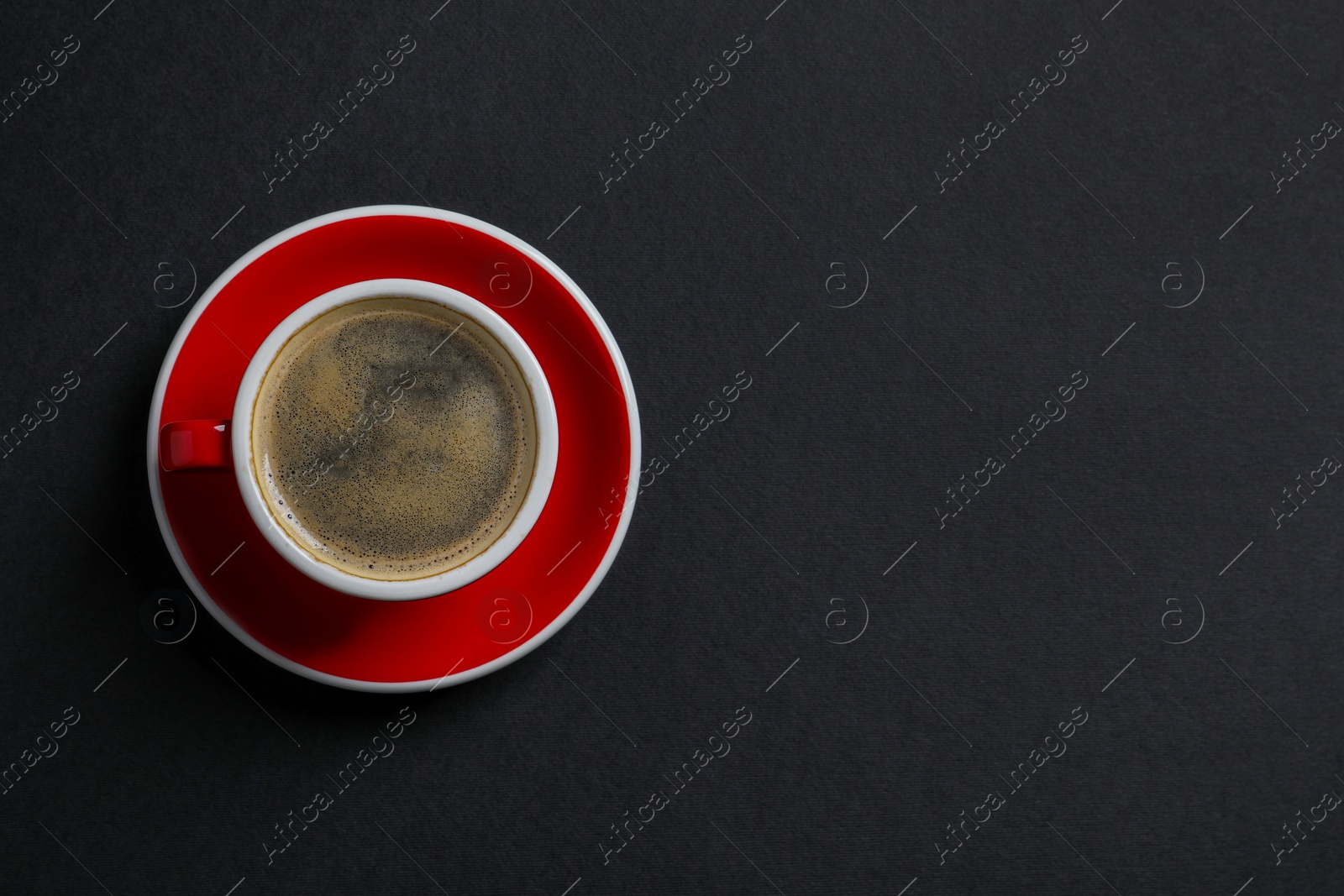 Photo of Red ceramic cup with hot aromatic coffee on black background, top view. Space for text