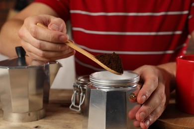 Photo of Man putting ground coffee into moka pot at wooden table, closeup