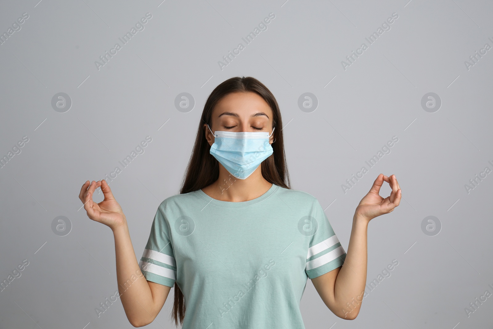 Photo of Woman in protective mask meditating on grey background. Dealing with stress caused by COVID‑19 pandemic