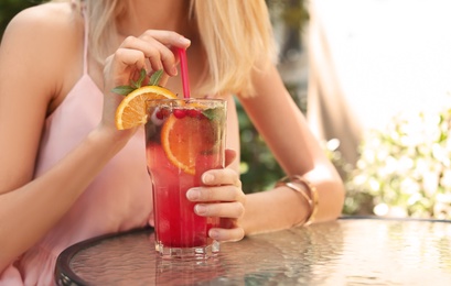 Young woman with glass of tasty natural lemonade at table in cafe, closeup. Detox drink