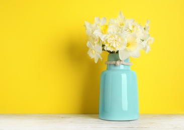 Photo of Bouquet of daffodils in vase on table against color background, space for text. Fresh spring flowers