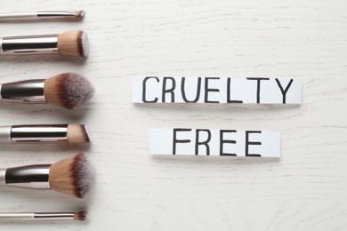 Photo of Cards with text Cruelty Free and makeup brushes on white wooden table, flat lay. Stop animal tests