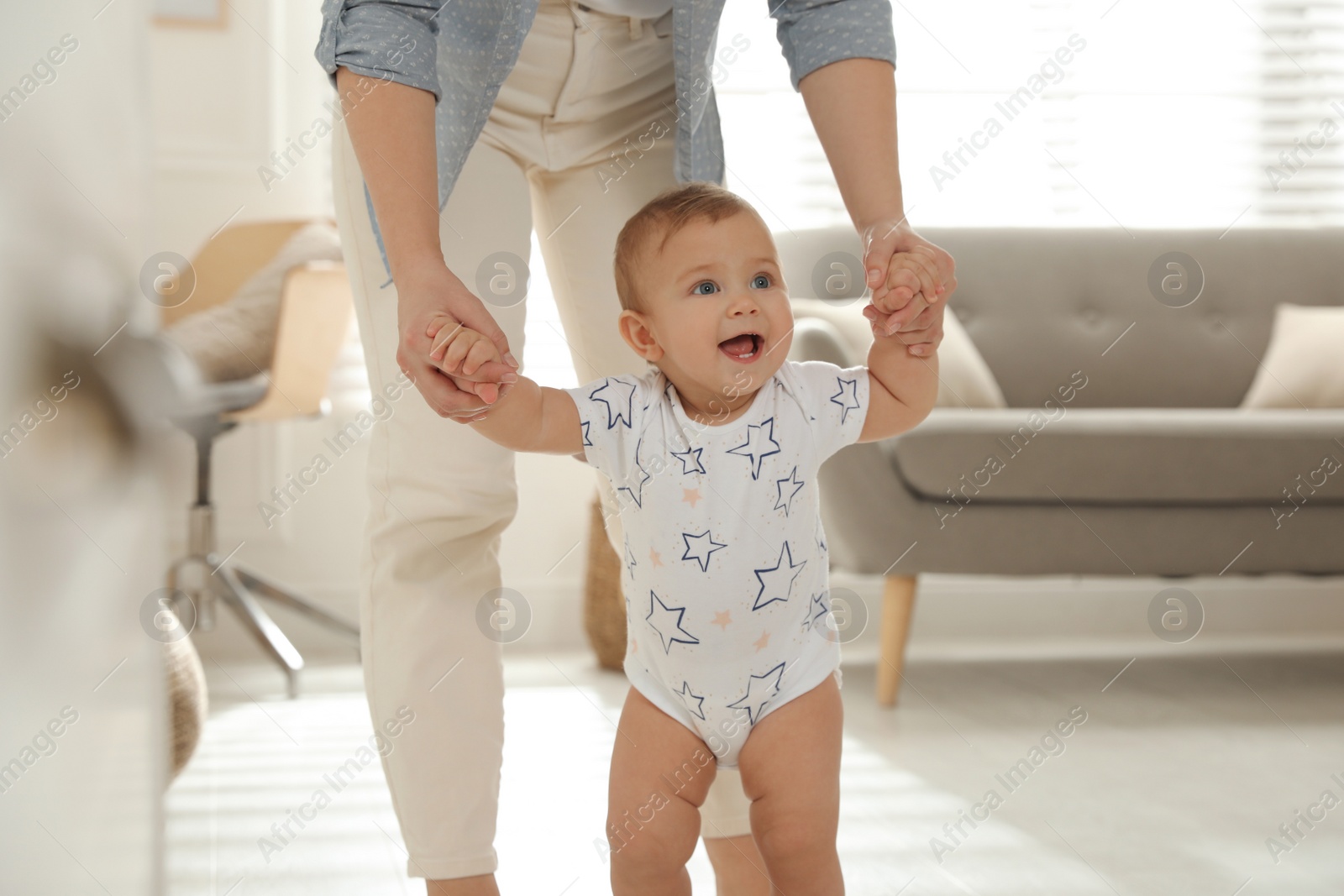 Photo of Mother supporting her baby daughter while she learning to walk at home