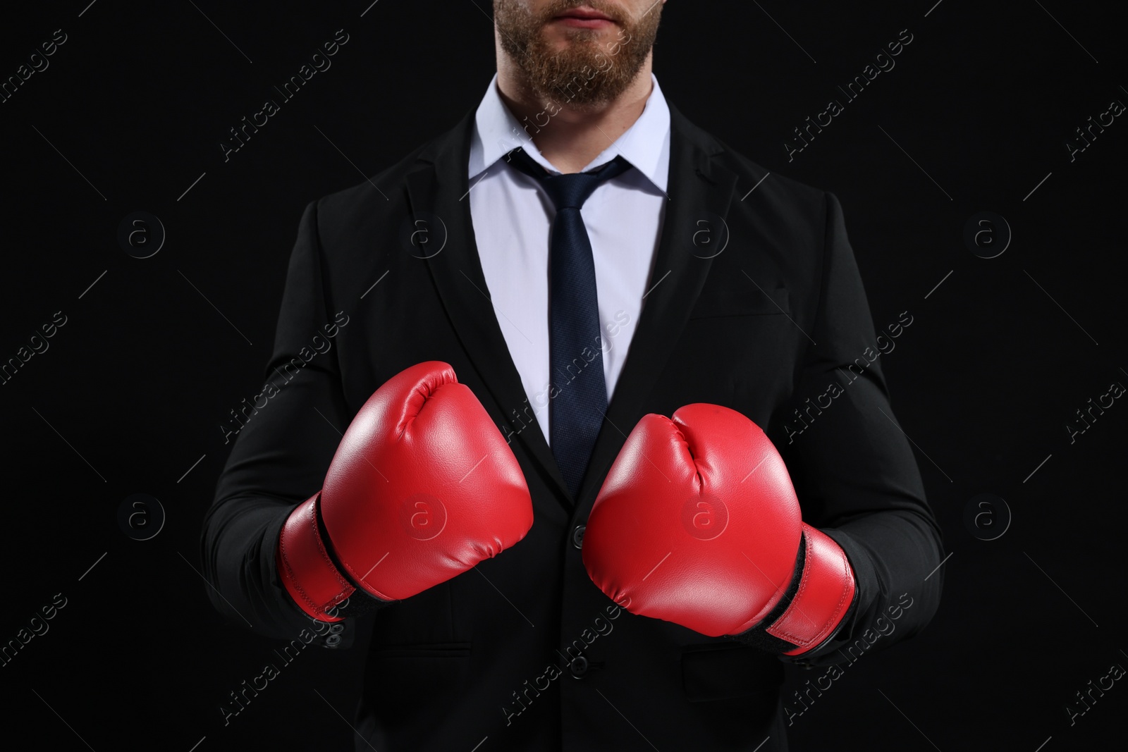 Photo of Businessman in suit wearing boxing gloves on black background, closeup