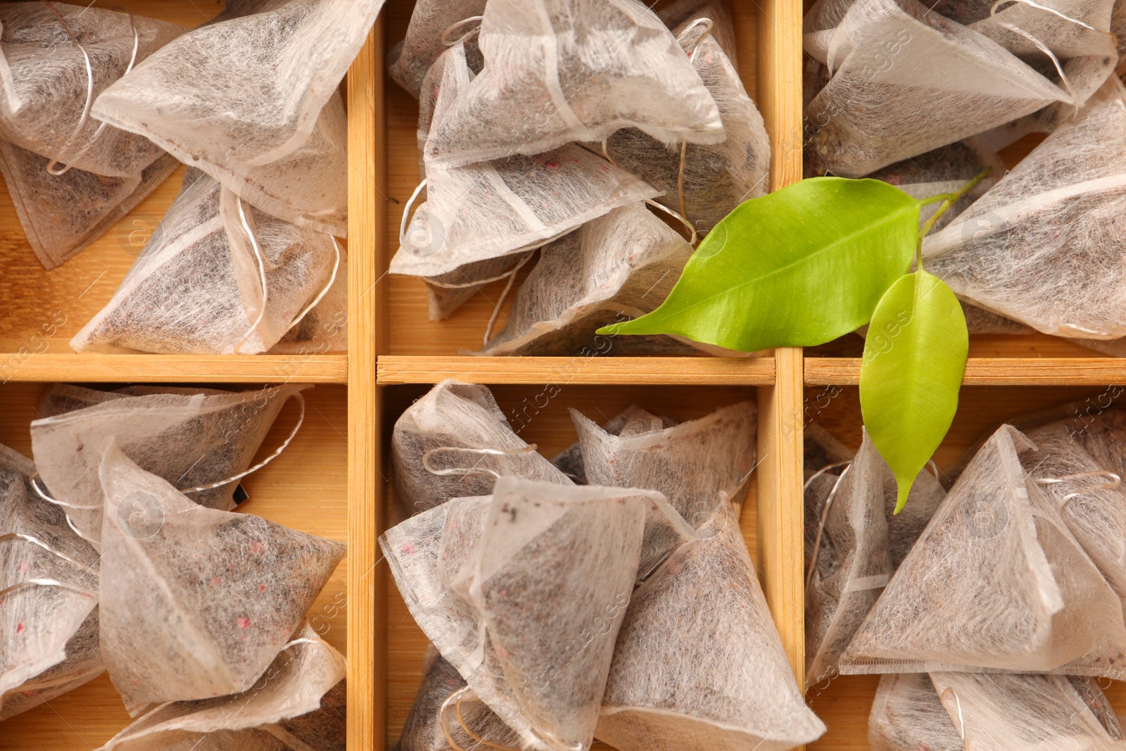 Photo of Many tea bags in wooden box as background, top view