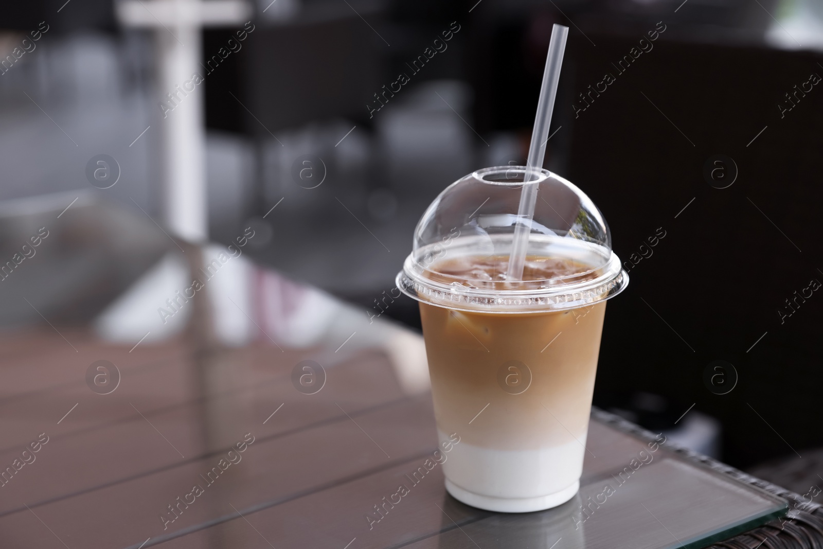 Photo of Plastic takeaway cup of delicious iced coffee on table in outdoor cafe, space for text